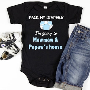 May include: Black baby onesie with the text "PACK MY DIAPERS" and "I'm going to Mawmaw & Papaw's house". The onesie has a blue diaper graphic. Includes a pair of black and white baby sneakers and a pair of blue jeans.