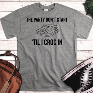 Könnte beinhalten: Graues T-Shirt mit dem Text "The party don't start 'til I croc in" und einer Schwarzweißillustration von zwei Paar Crocs.