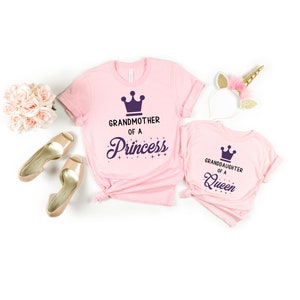 May include: Two pink t-shirts with a crown graphic and text. The larger shirt says "Grandmother of a Princess" and the smaller shirt says "Granddaughter of a Queen".