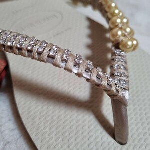 May include: Beige flip-flops with a decorative strap adorned with small rhinestones and pearl-like beads.