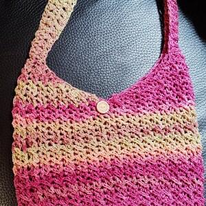 May include: A crocheted tote bag with a pink, green, and beige color gradient. The bag has a single button closure.