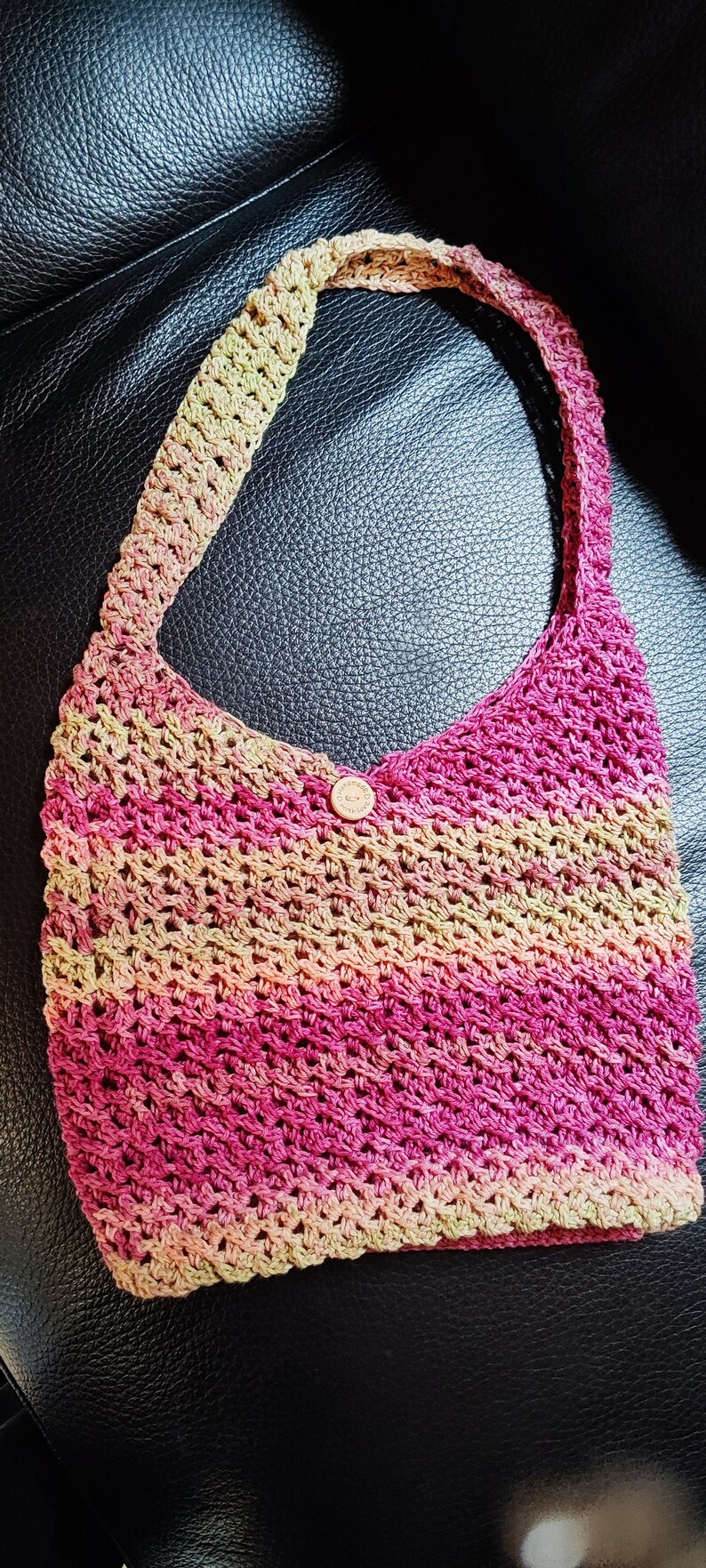 May include: A crocheted tote bag with a pink, green, and beige color gradient. The bag has a single button closure.