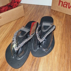 May include: A pair of black flip-flops with clear straps and a silver rhinestone embellishment.