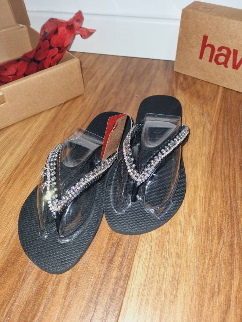 May include: A pair of black flip-flops with clear straps and a silver rhinestone embellishment.