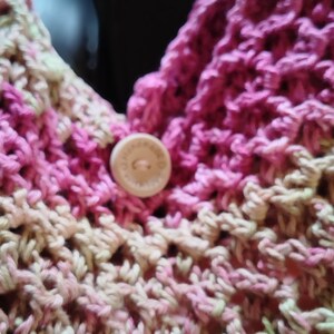 May include: Close-up of a pink and green crocheted bag with a wooden button.