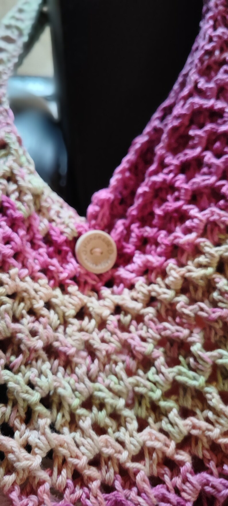 May include: Close-up of a pink and green crocheted bag with a wooden button.
