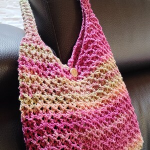 May include: A crocheted handbag with a pink, green, and beige ombre pattern. The bag has a single button closure.