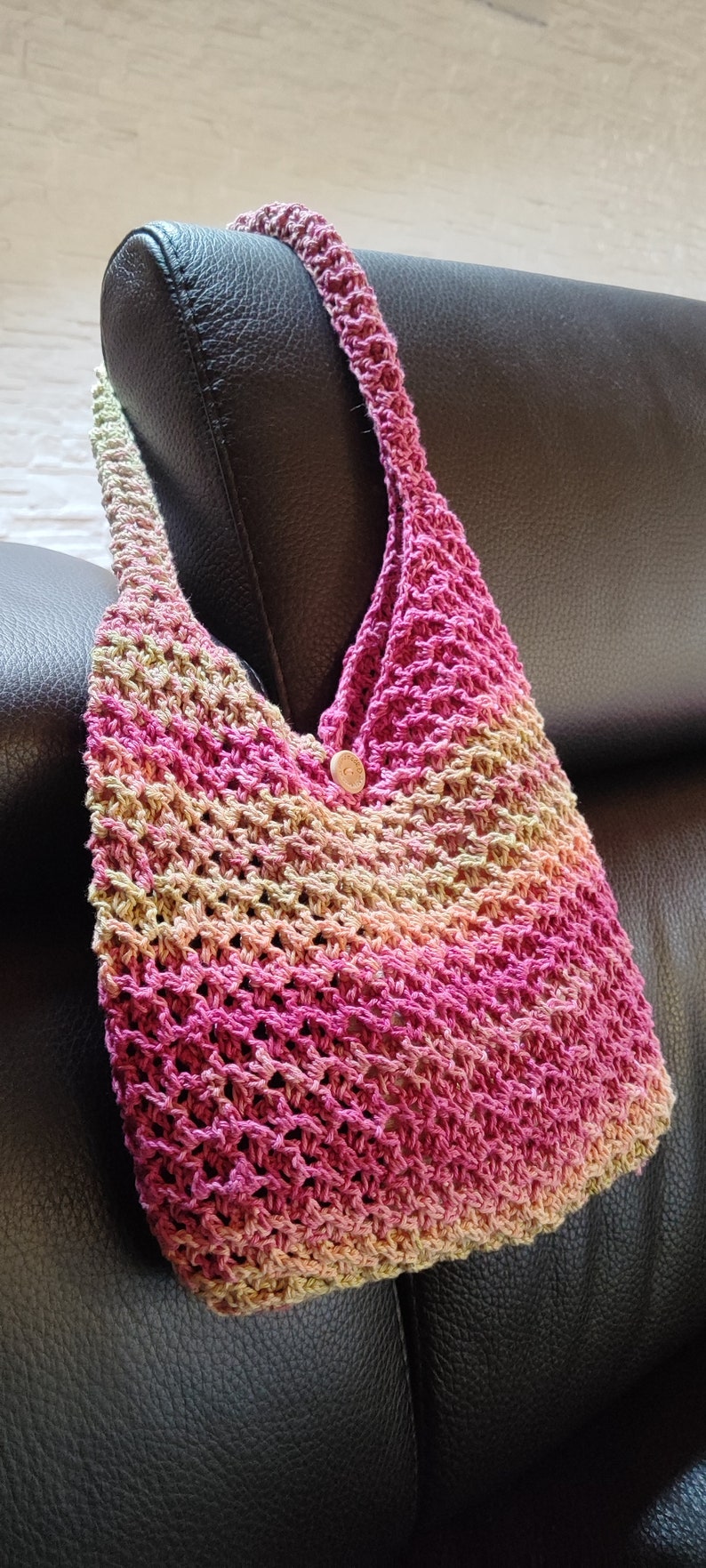 May include: A crocheted handbag with a pink, green, and beige ombre pattern. The bag has a single button closure.