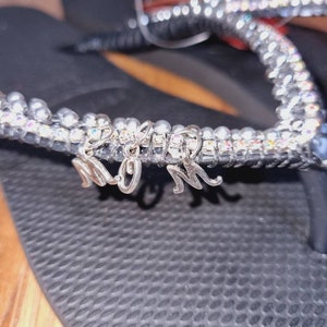 May include: Black flip flops with a silver rhinestone strap and a silver charm that says "MOM".