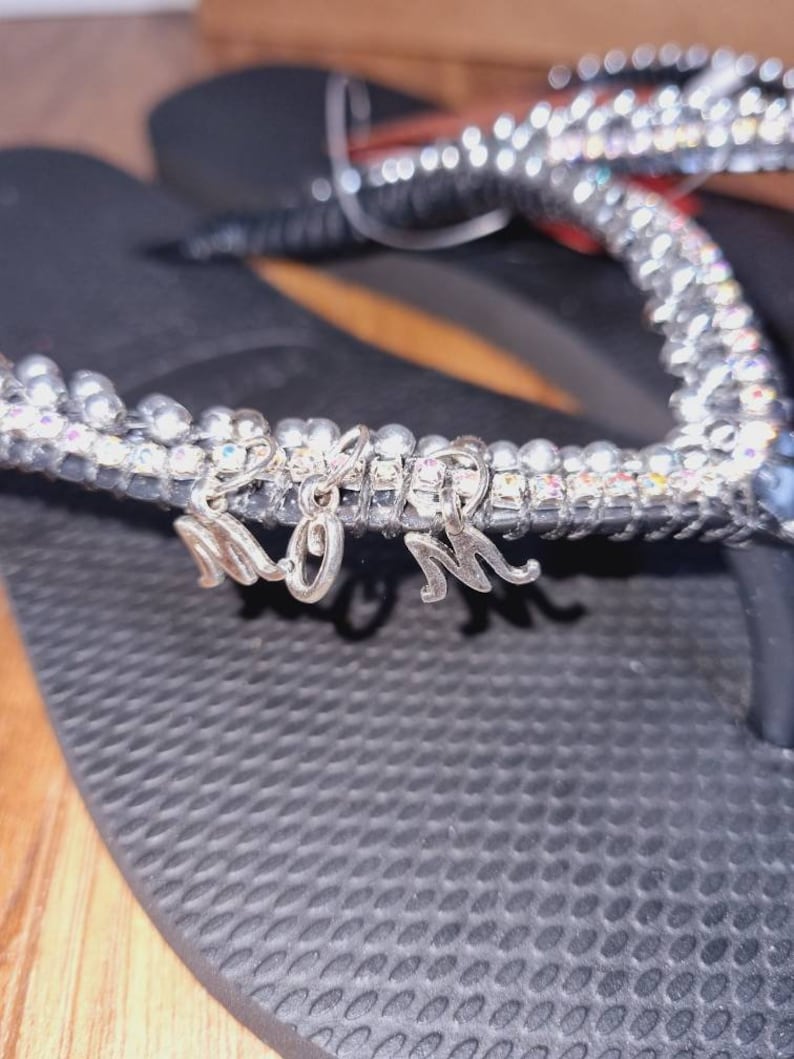 May include: Black flip flops with a silver rhinestone strap and a silver charm that says "MOM".