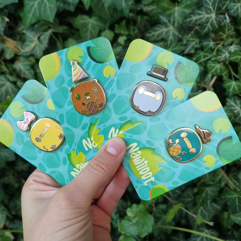 May include: Four enamel pins featuring cartoon animal characters on a green and yellow background. The pins are on cards with the text "Newloot" printed on them. The characters are a beaver wearing a party hat, a penguin wearing a top hat, a turtle wearing a hat, and a duck wearing a bow.