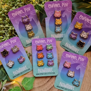 May include: Set of enamel pins featuring different colored frogs with the text "Nawiloot Enamel Pin" and the website address "www.nawiloot.etsy.com".