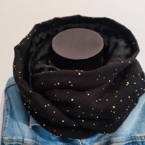 Peut inclure: Écharpe noire infinie avec des points de paillettes dorés. L'écharpe est pliée et présentée sur une veste en jean.