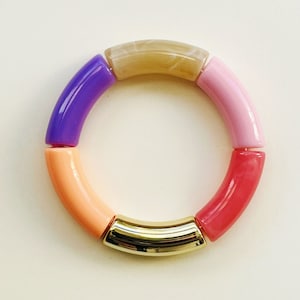 Könnte beinhalten: Ein farbenfrohes Armband mit sechs Perlen. Die Perlen sind in den Farben Rosa, Orange, Lila und Beige. Das Armband hat einen goldenen Metallverschluss.