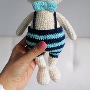 May include: White crocheted bunny toy wearing blue and white striped overalls with a light blue bow tie.
