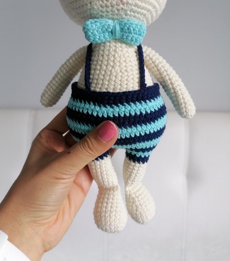 May include: White crocheted bunny toy wearing blue and white striped overalls with a light blue bow tie.