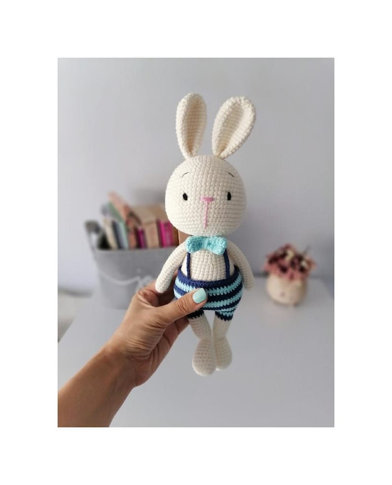 May include: A white crocheted bunny wearing blue and light blue striped overalls with a light blue bow tie.