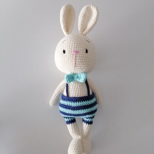 May include: White crocheted bunny rabbit wearing blue and turquoise striped overalls with a turquoise bow tie.
