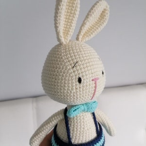 May include: A white crocheted bunny wearing a blue and white striped outfit with a blue bow tie.