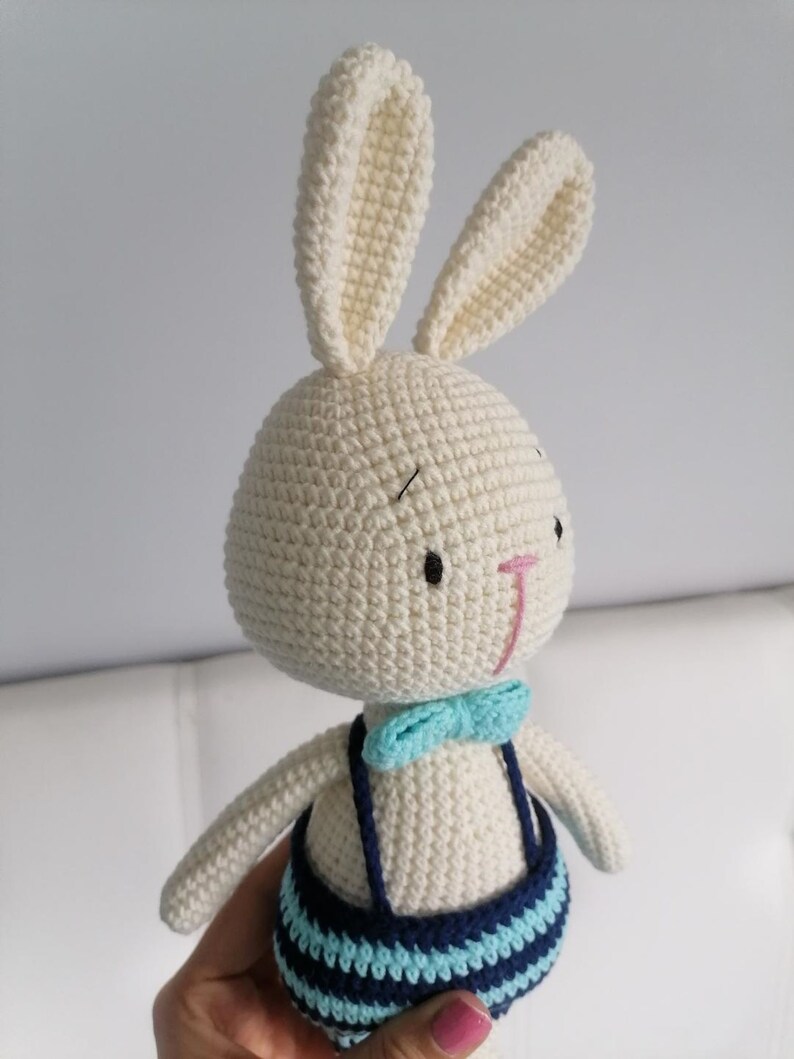 May include: A white crocheted bunny wearing a blue and white striped outfit with a blue bow tie.