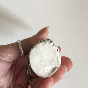 Puede incluir: Figura de cer&aacute;mica blanca de un gato sentado con lunares negros. La figura mide aproximadamente 7,5 cm de alto y tiene un acabado liso y mate.