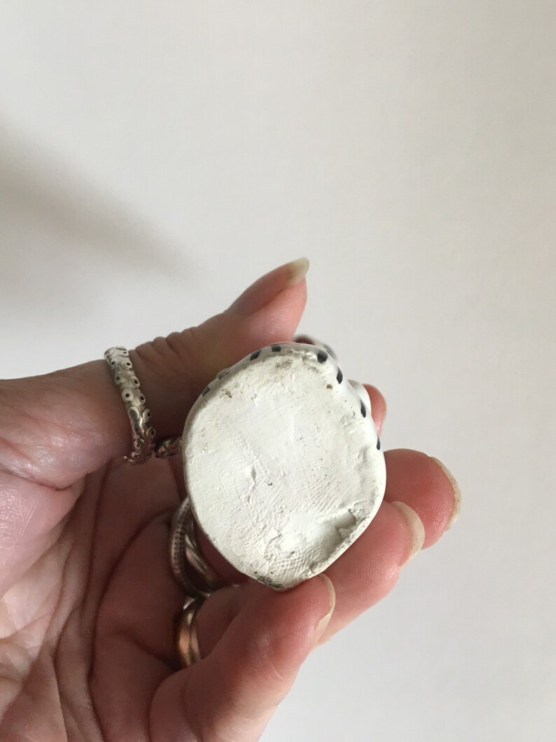 Puede incluir: Figura de cer&aacute;mica blanca de un gato sentado con lunares negros. La figura mide aproximadamente 7,5 cm de alto y tiene un acabado liso y mate.