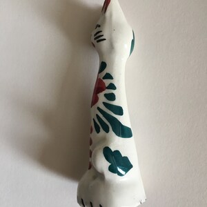 Puede incluir: Figura de cer&aacute;mica blanca de un gato con dise&ntilde;os florales verdes y rojos. El gato est&aacute; de pie con la cabeza levantada.