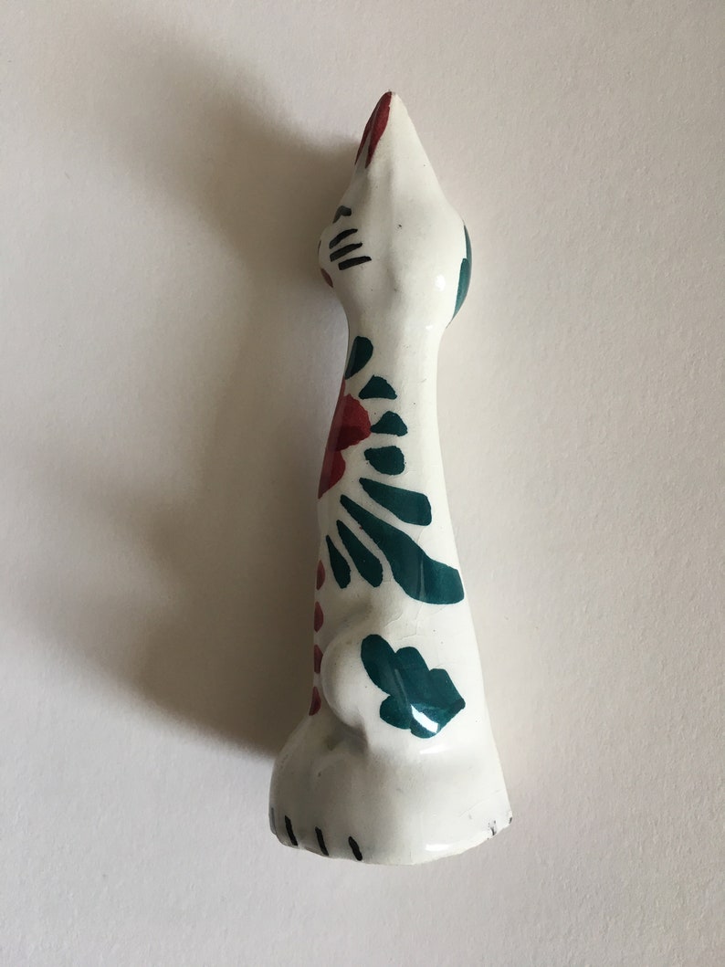 Puede incluir: Figura de cer&aacute;mica blanca de un gato con dise&ntilde;os florales verdes y rojos. El gato est&aacute; de pie con la cabeza levantada.