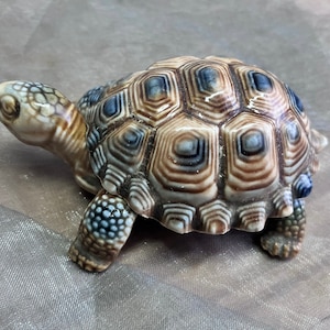 May include: A ceramic turtle figurine with a brown and blue patterned shell. The turtle is in a walking position with its head turned to the side.