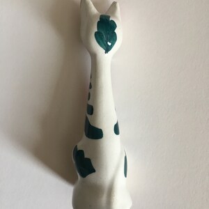 Puede incluir: Figura de cer&aacute;mica blanca de un gato con manchas pintadas de verde y un dise&ntilde;o de hoja verde en la espalda.