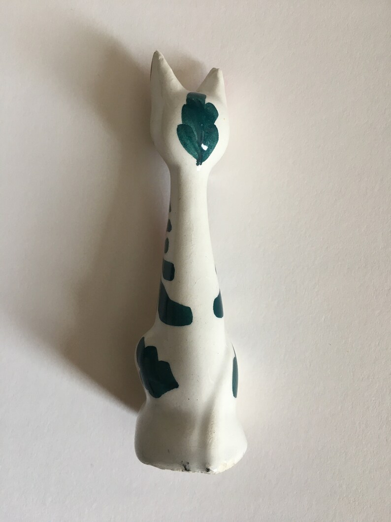 Puede incluir: Figura de cer&aacute;mica blanca de un gato con manchas pintadas de verde y un dise&ntilde;o de hoja verde en la espalda.