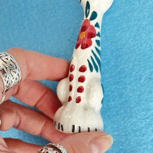 Puede incluir: Figura de cer&aacute;mica blanca de un gato con dise&ntilde;os florales verdes y rojos. El gato est&aacute; de pie con la cabeza inclinada hacia arriba.
