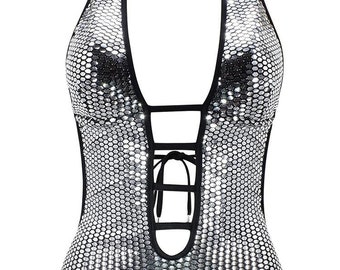May include: A silver sequined halter top with a black halter strap and a tie at the neck. The top has a deep V-neckline and a lace-up detail at the center.