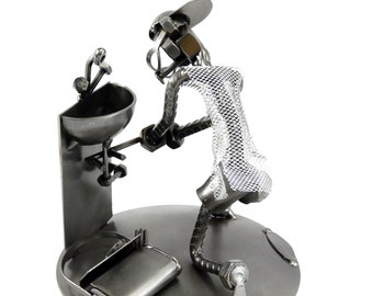 May include: A metal sculpture of a person in a golf pose, made from nuts, bolts, and other metal pieces. The sculpture is holding a golf club and is wearing a hat. The sculpture is standing on a round base.