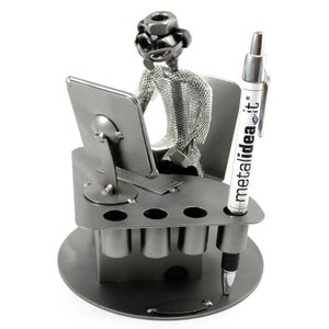 Op de afbeelding: Een zilveren metalen bureau-organizer in de vorm van een persoon die aan een computer zit. De organizer heeft een pennenhouder, een potloodhouder en een klein vakje om paperclips of andere kleine items in te bewaren. De organizer is gemaakt van metaal en heeft een zilveren afwerking. De organizer is een geweldige manier om je bureau georganiseerd en opgeruimd te houden. De organizer heeft de tekst "metalidea.it" op de pennenhouder.