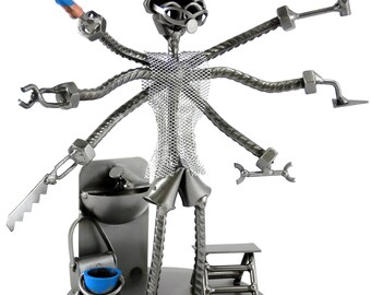 May include: A metal sculpture of a person with multiple arms holding various tools, including a saw, wrench, hammer, and paintbrush. The sculpture is standing on a base with a bucket and a small ladder.