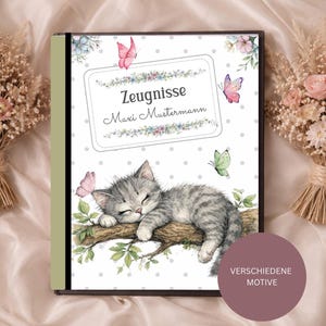 Könnte beinhalten: Ein Notizbuch mit einer Aquarellillustration eines schlafenden grauen Tabby-Kätzchens auf einem Ast, umgeben von Schmetterlingen und Blumen. Auf dem Cover steht der Text "Zeugnisse Maxi Mustermann". Das Notizbuch wird auf einem weichen, hellen Stoff präsentiert.