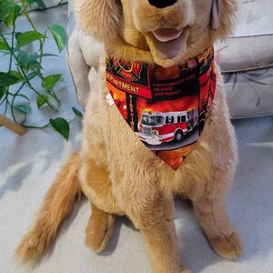 May include: A plush golden retriever dog wearing a red and black bandana with a fire truck and the text "Firefighters Save Hearts and Homes" and "Department".