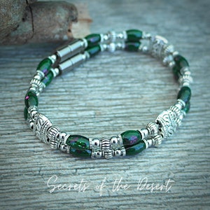 May include: A double-strand bracelet with green and silver beads. The bracelet has a magnetic clasp and features a decorative silver bead with an ornate design.