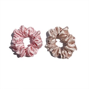 May include: Two satin scrunchies. One is a light pink color, and the other is a light tan color. The scrunchies are round and have a gathered, ruffled appearance. They are set against a white background.