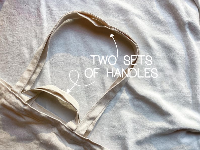 May include: A beige canvas tote bag with two sets of handles. The bag is folded in half and the handles are visible.