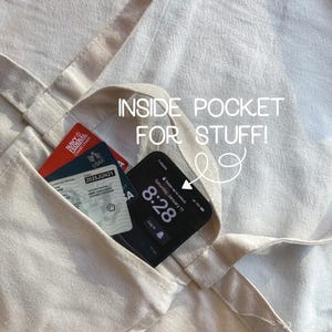 May include: A beige tote bag with an inside pocket. The pocket contains a credit card and a smartphone with the time 8:28 displayed on the screen. The text "INSIDE POCKET FOR STUFF!" is written on the bag.