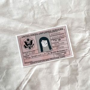 May include: A sticker designed to look like a United States Uniformed Services ID card. It features a cartoon illustration, text, and the phrase "Do you know who my spouse is??" in pink and white. The expiration date is 2022DEC31.