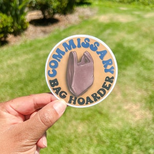 Op de afbeelding: Een ronde sticker met een bruine plastic tas en de tekst "Commissary Bag Hoarder" in blauwe en witte letters op een gele achtergrond.