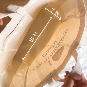 May include: A white canvas tote bag with a brown logo that says "I  comma  love  nature" and a brown leaf design. The bag measures 15 inches wide and 7 inches tall.
