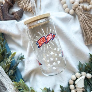 May include: Clear glass tumbler with a bamboo lid and a clear straw. The tumbler features a "Coast Guard" graphic in red, white, and blue, along with white star accents. The tumbler is designed for cold beverages.