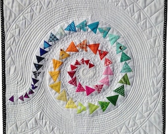 May include: A white quilt featuring a colourful spiral design made of fabric triangles. The spiral is surrounded by concentric circles of stitching.