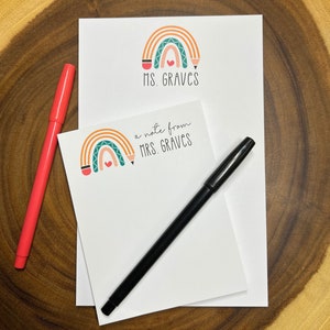May include: Two white notepads with a rainbow, pencil, and heart design. The top notepad says "Ms. Graves" and the bottom notepad says "a note from Mrs. Graves".