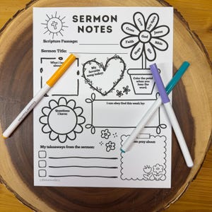 May include: A black and white sermon notes sheet with floral and heart designs, and the text "SERMON NOTES". Three markers in orange, purple, and teal are on the sheet. The sheet is on a wooden surface.