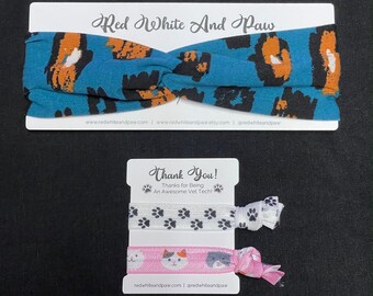 May include: A thank you card with a blue and orange patterned headband and two hair scrunchies. The scrunchies have paw prints and a cat design. The card says "Thank You! Thanks for Being An Awesome Vet Tech!" and includes the website address redwhiteandpaw.com.